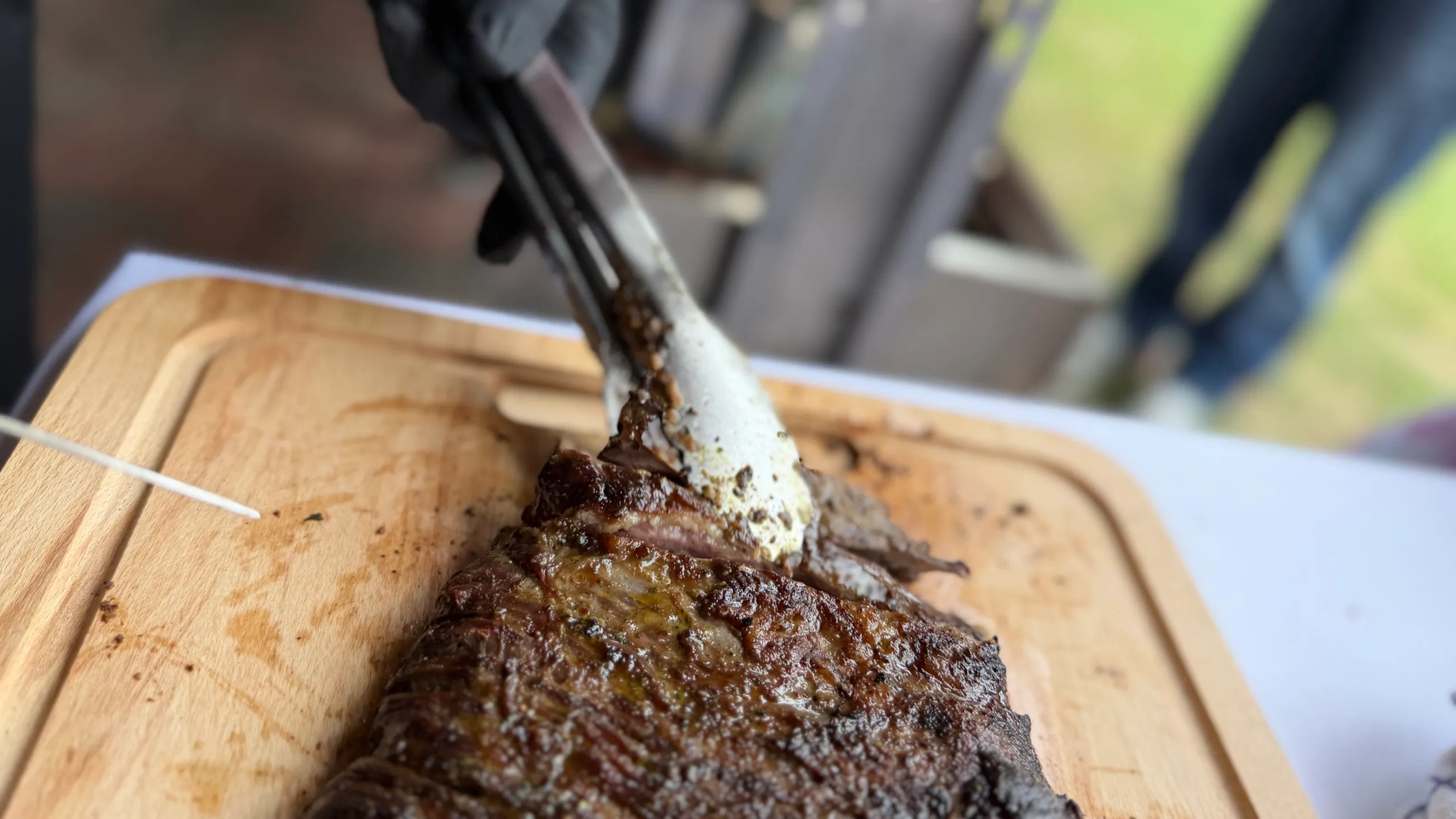 Gegrilltes Steak wird mit der Zange auf dem Schneidebrett angerichtet